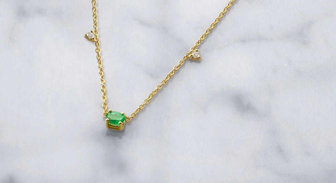 Oval emerald stone necklace with diamond stations on marble background- Camille Jewelry
