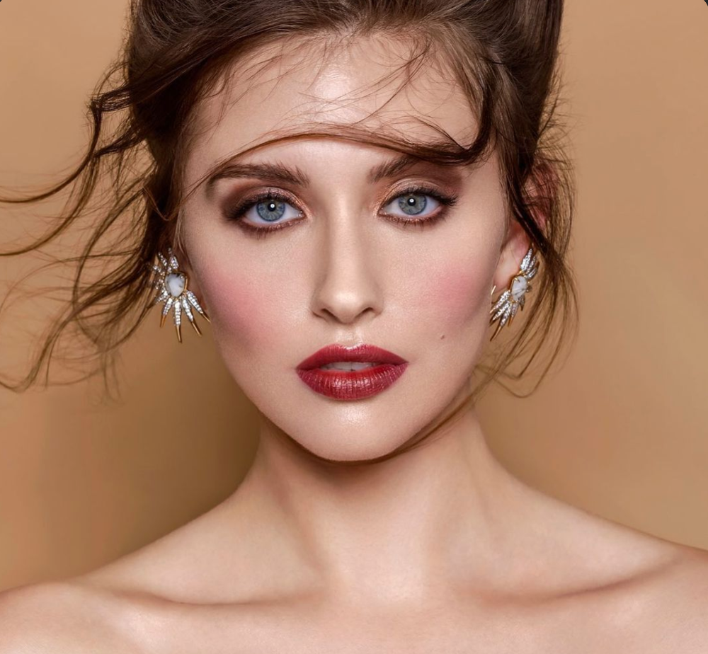 Close-up of a woman wearing diamond earrings against a beige background