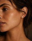 Close-up of a woman wearing a round pave diamond stud earrings with a warm, soft focus background by Camille Jewelry.