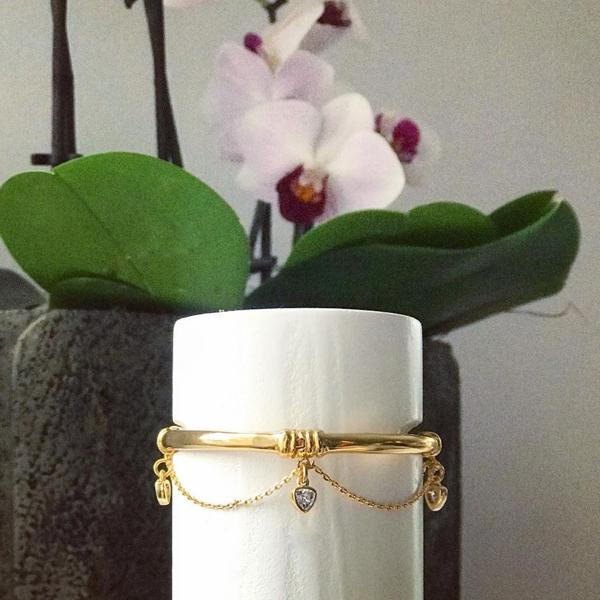 Close up of Thyra Gold Charm Swag Bracelet in Gold in front of white flower