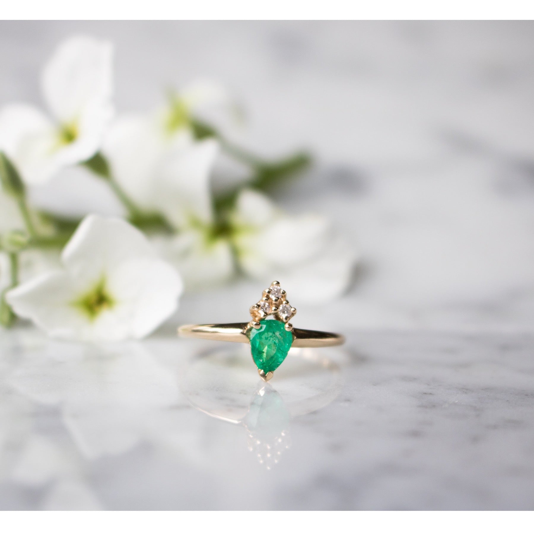 Close up view of the Venus 14K Gold Emerald Pear Ring with Diamonds on white granite background