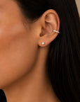 Close-up of a model wearing Camille Jewelry 14K solid gold diamond cuff earrings, styled with a small pearl stud for a delicate ear stack look.