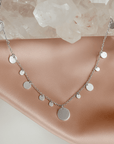 Silver plated disc charm convertible necklace and eyeglass chain displayed on a quartz stone and soft pink background by Camille Jewelry.