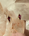 Pair of kite cut lab created ruby gemstone stud earrings in 14K yellow gold on a quartz crystal background by Camille Jewelry