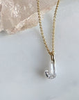 A delicate 14k yellow gold chain necklace with a floating lab created diamond "J" initial charm resting on a light marble surface next to a pink crystal cluster, by Camille Jewelry