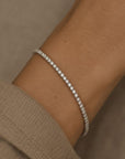 Woman wearing a lab grown diamond tennis bracelet in 14K white gold on a wrist against a neutral background by Camille Jewelry