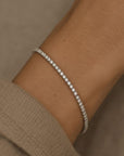 Woman wearing a lab grown diamond tennis bracelet in 14K white gold on a wrist against a neutral background by Camille Jewelry
