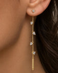 A close-up of a model's ear wearing a gold dangle linear earring with trillion shaped cubic zirconia charms and a gold tube at the end by Camille Jewelry.