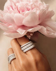 Hand wearing two pave sterling silver square rings with a pink flower in the background, by Camille Jewelry.
