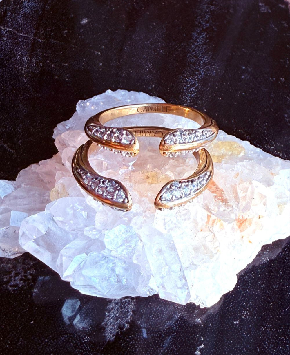 Gold ring with diamonds on a crystal surface, branded 'Camille Jewelry'.