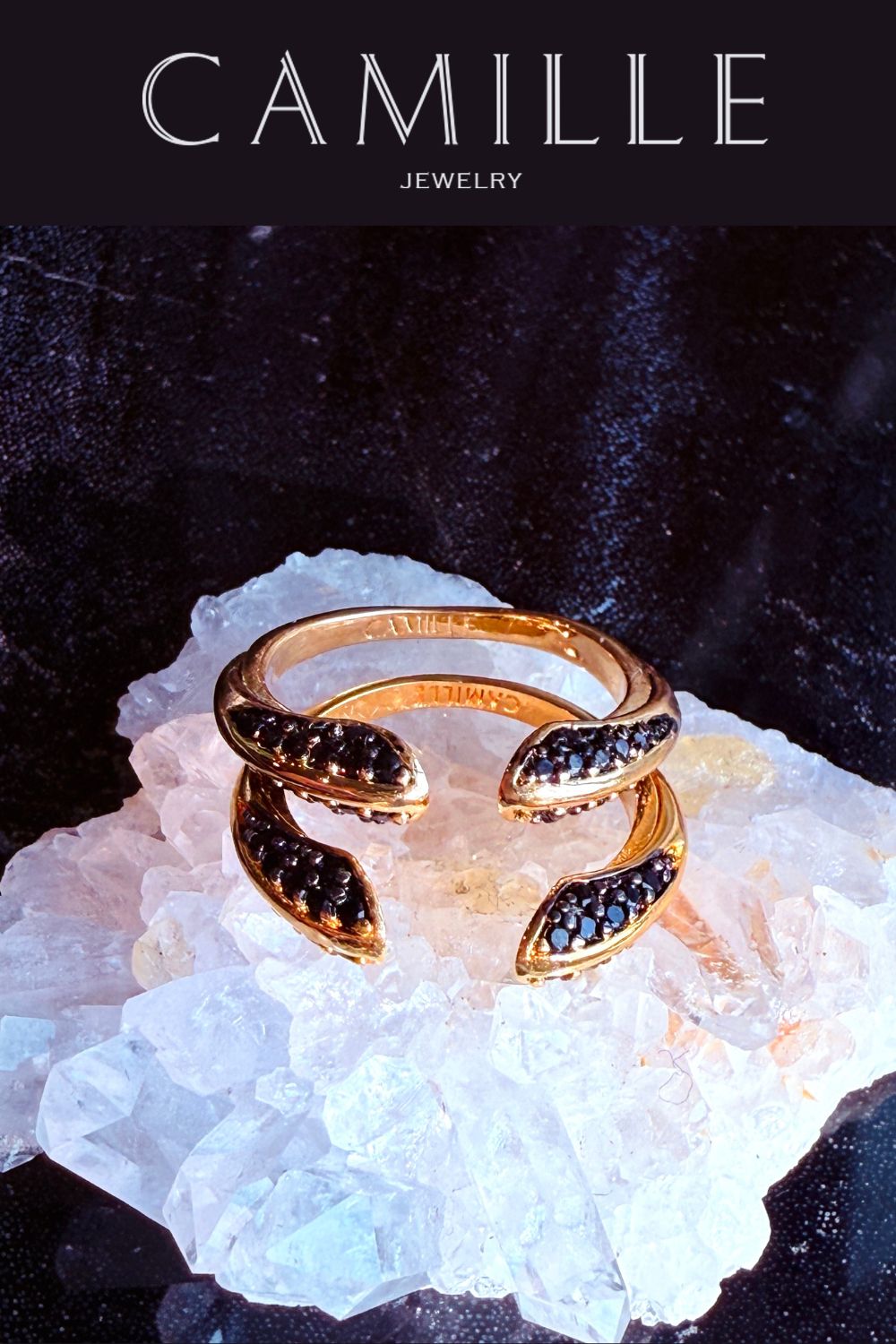 Gold ring with black spinel gemstones on a white crystal base, branded as Camille Jewelry.
