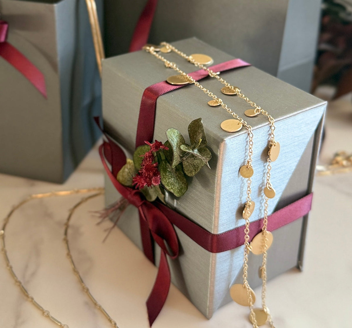 Holiday gift guide 2026 showcasing a silk silver jewelry box with gold necklace and burgundy ribbon on a marble surface by Camille Jewelry