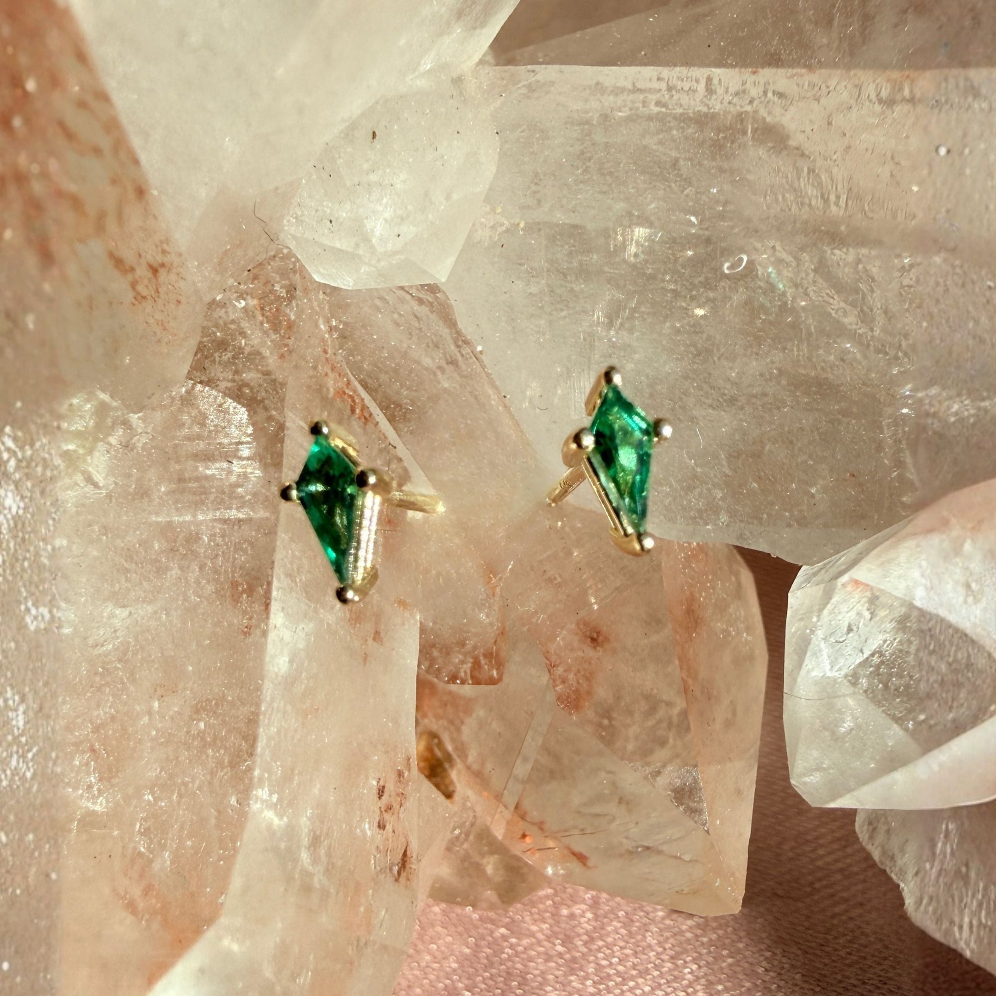 Pair of kite cut lab created emerald gemstone stud earrings in 14K yellow gold on a quartz crystal background by Camille Jewelry