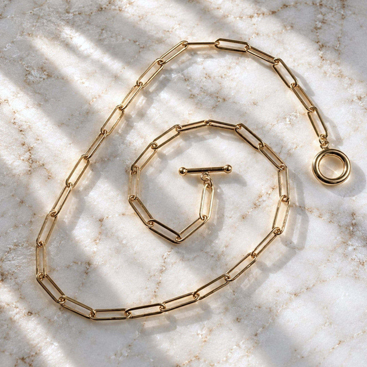 14k gold filled paperclip chain necklace on a marble background with natural sunlight, by Camille Jewelry