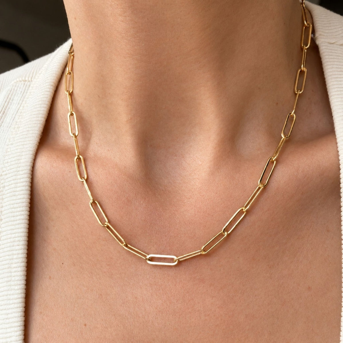 A close-up of a 14k gold filled paperclip chain necklace worn on a model's neck, styled with a cream-colored knit top, by Camille Jewelry