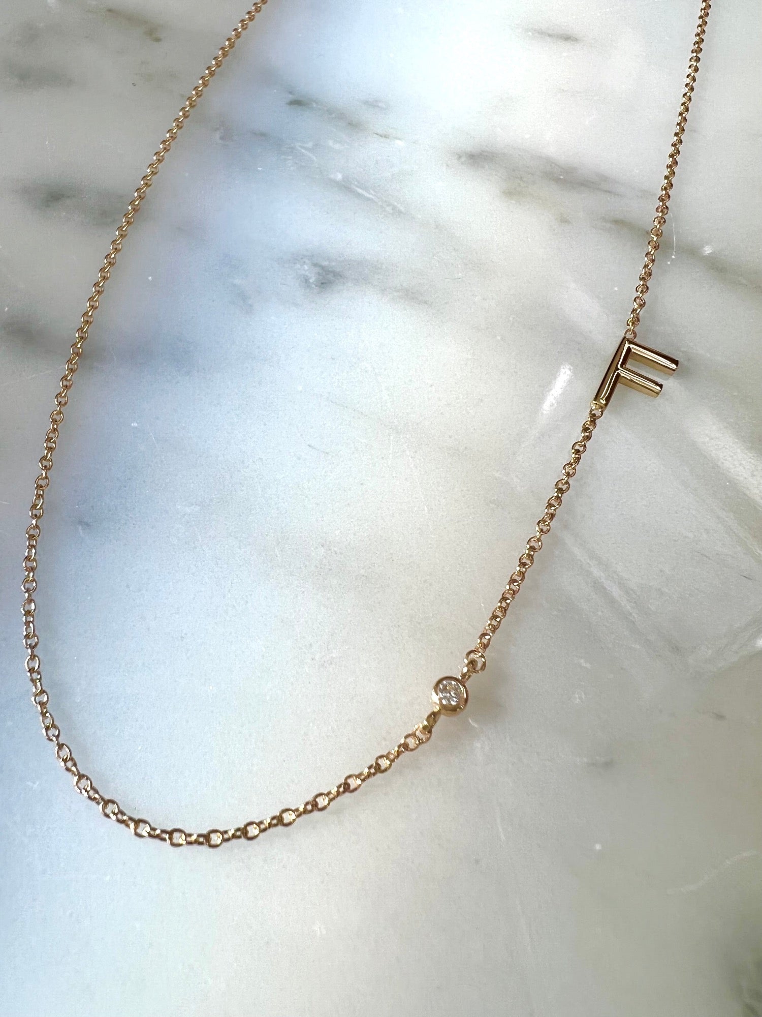 14k yellow gold delicate initial necklace with diamond accent on display by Camille Jewelry