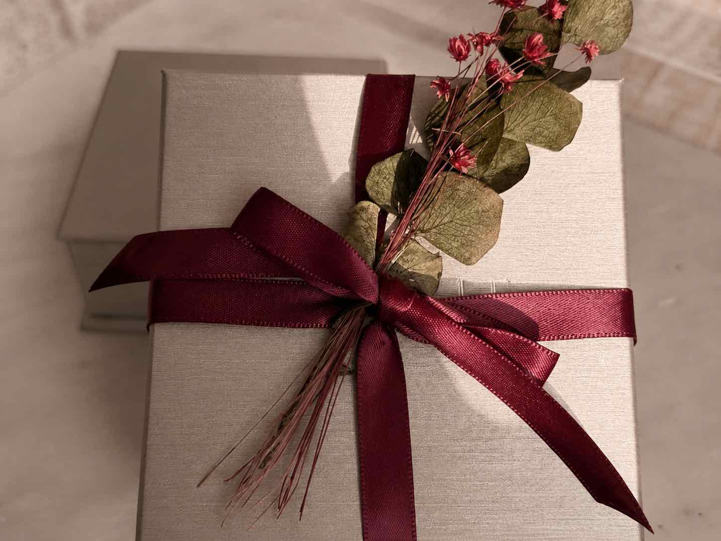 Designer Gifts box with a red ribbon and decorative leaves on a neutral background by Camille Jewelry