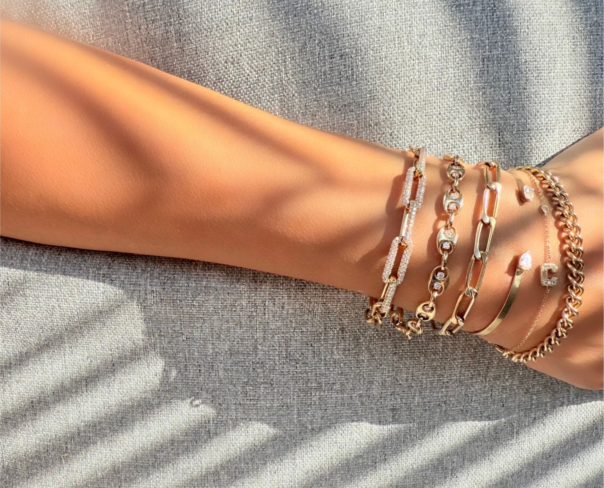 Gold and diamond bracelets on a wrist with a neutral background by Camille Jewelry. 