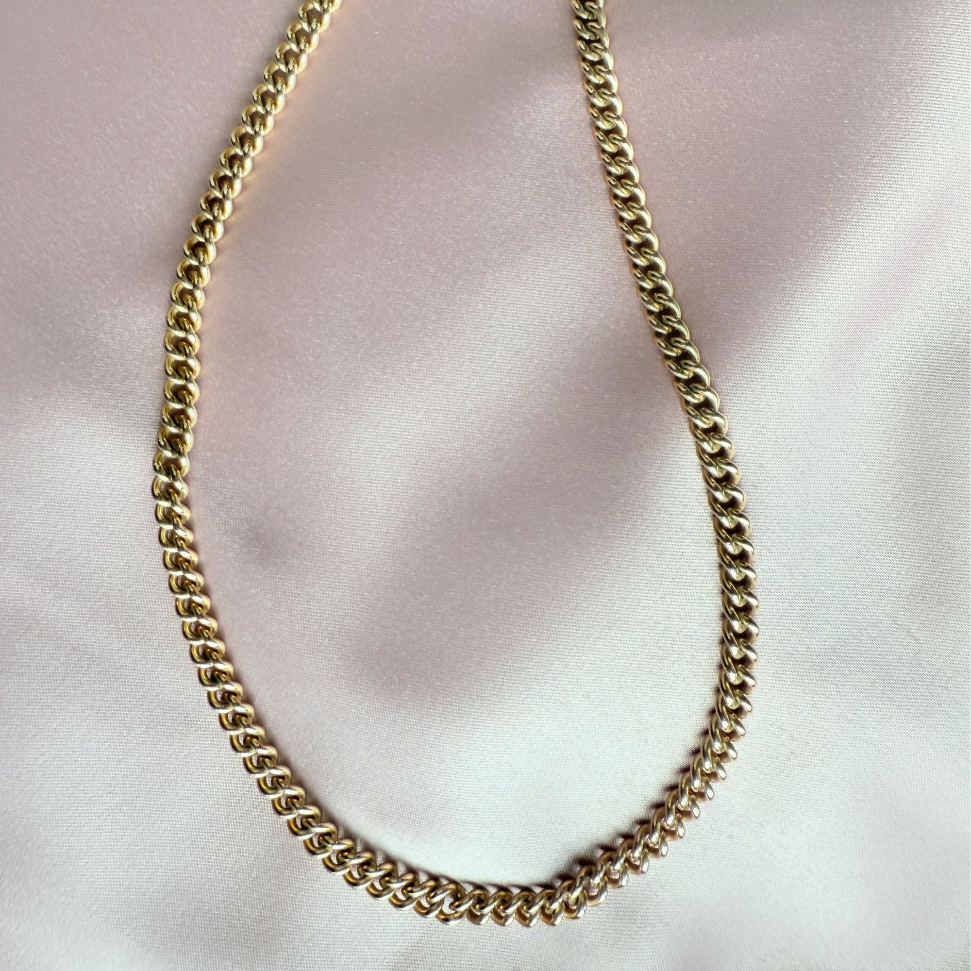 Gold filled curb chain necklace on a light pink fabric background
