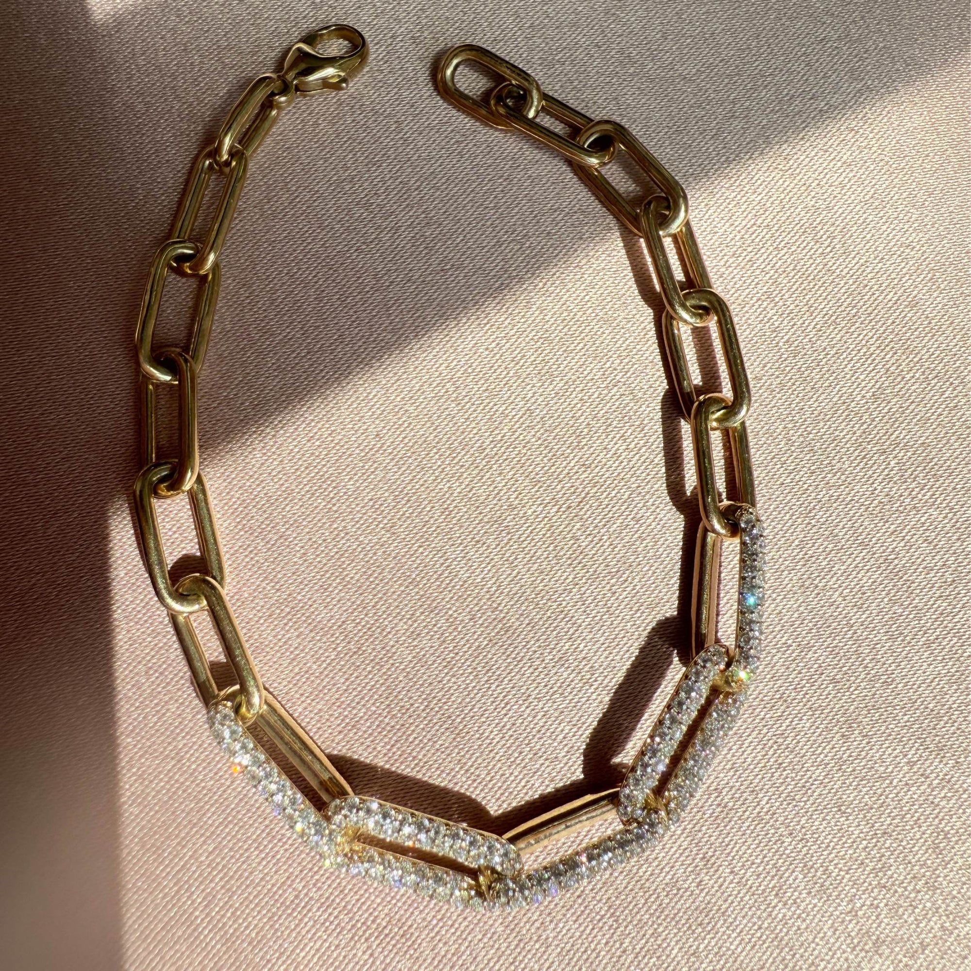 Yellow gold paperclip bracelet with diamond accents on a beige background by Camille Jewelry