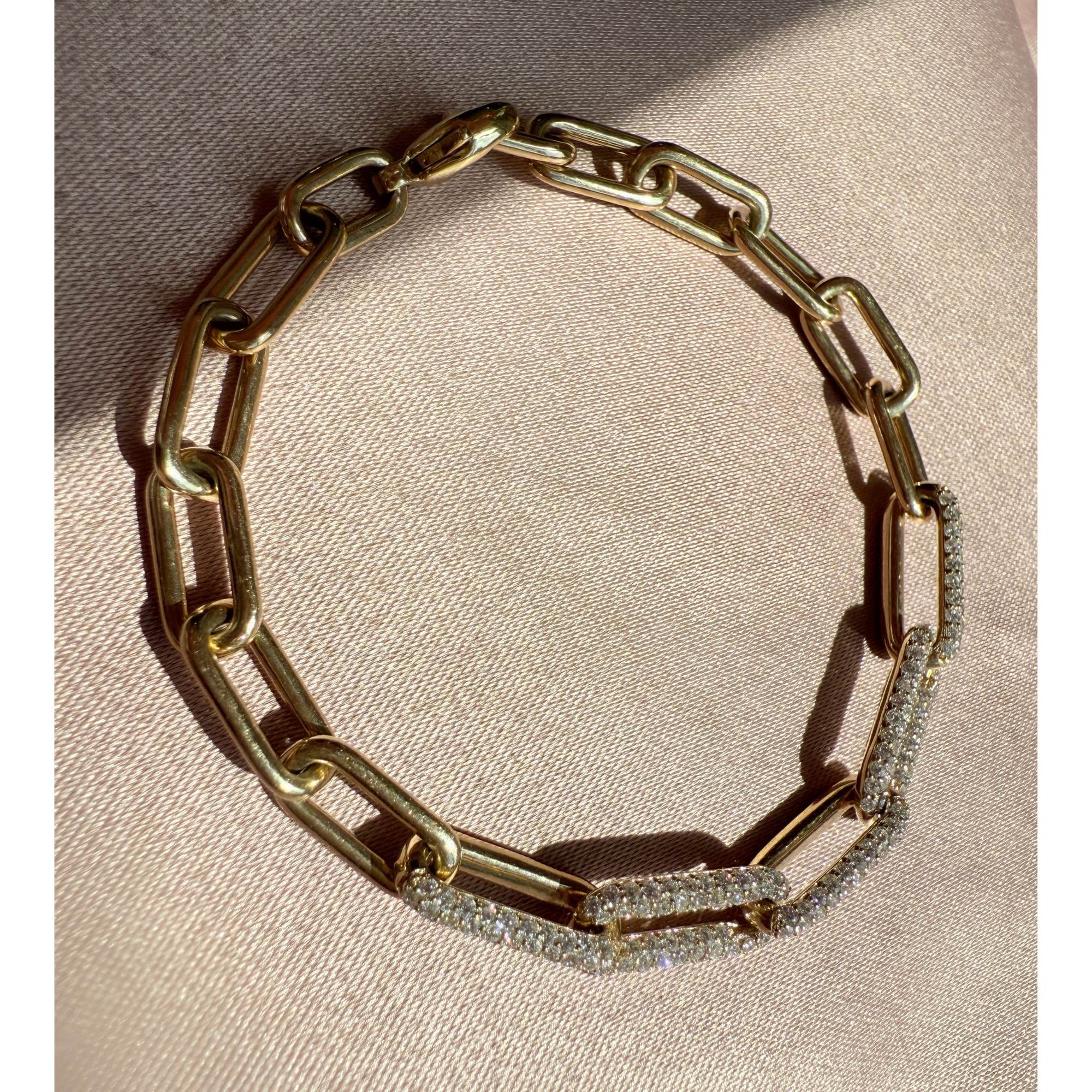 Gold paperclip bracelet with diamond accents on a beige fabric background by Camille Jewelry