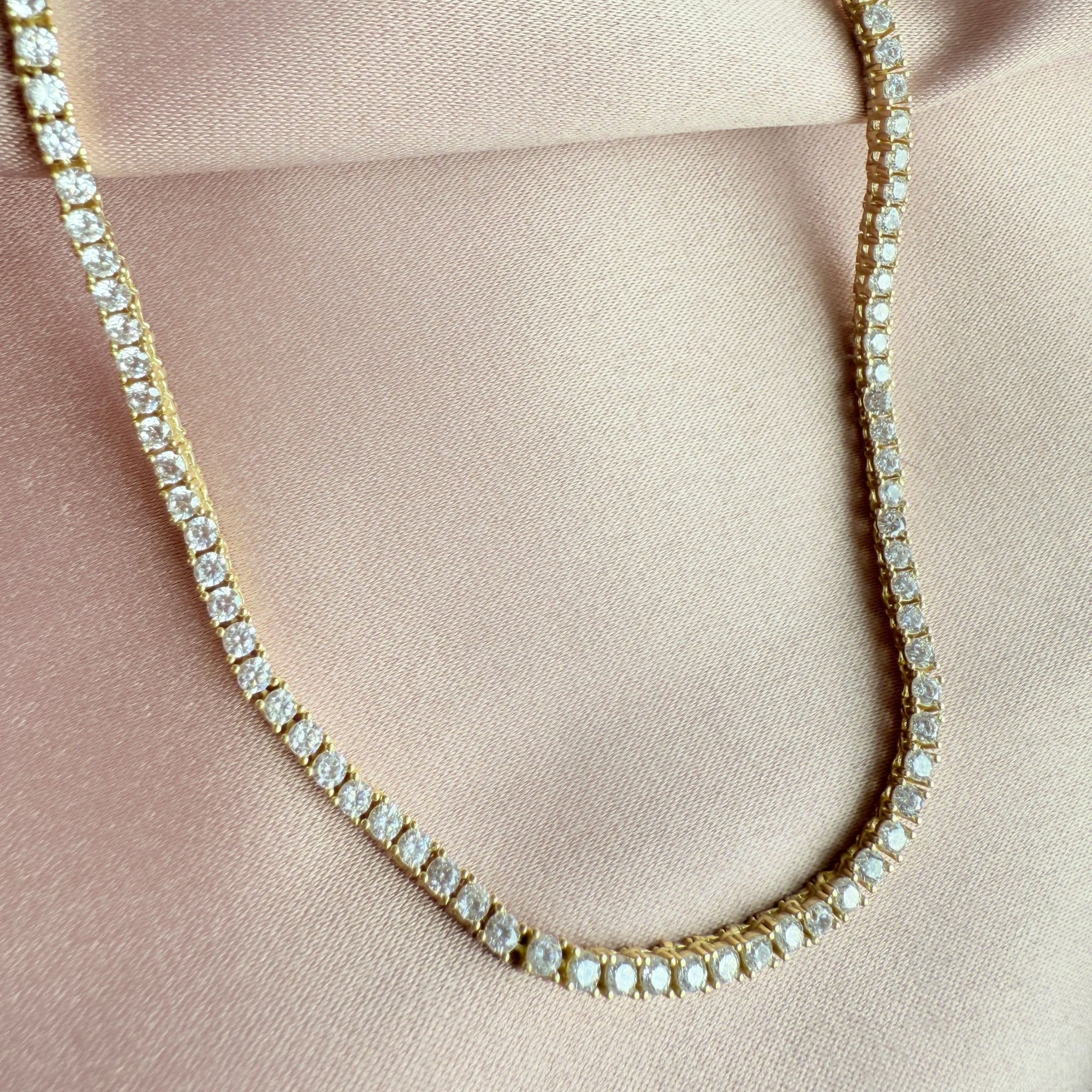 Gold tennis necklace with clear stones on a pink fabric background