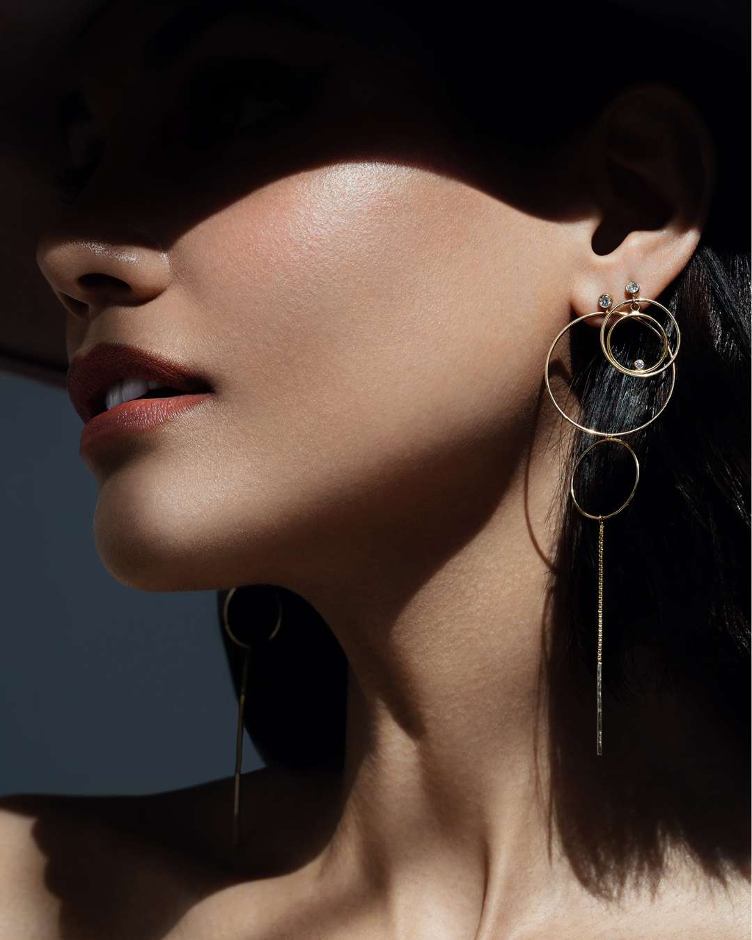 Close-up of a woman wearing long gold filled hoop earrings with a dark background by Camille Jewelry. 