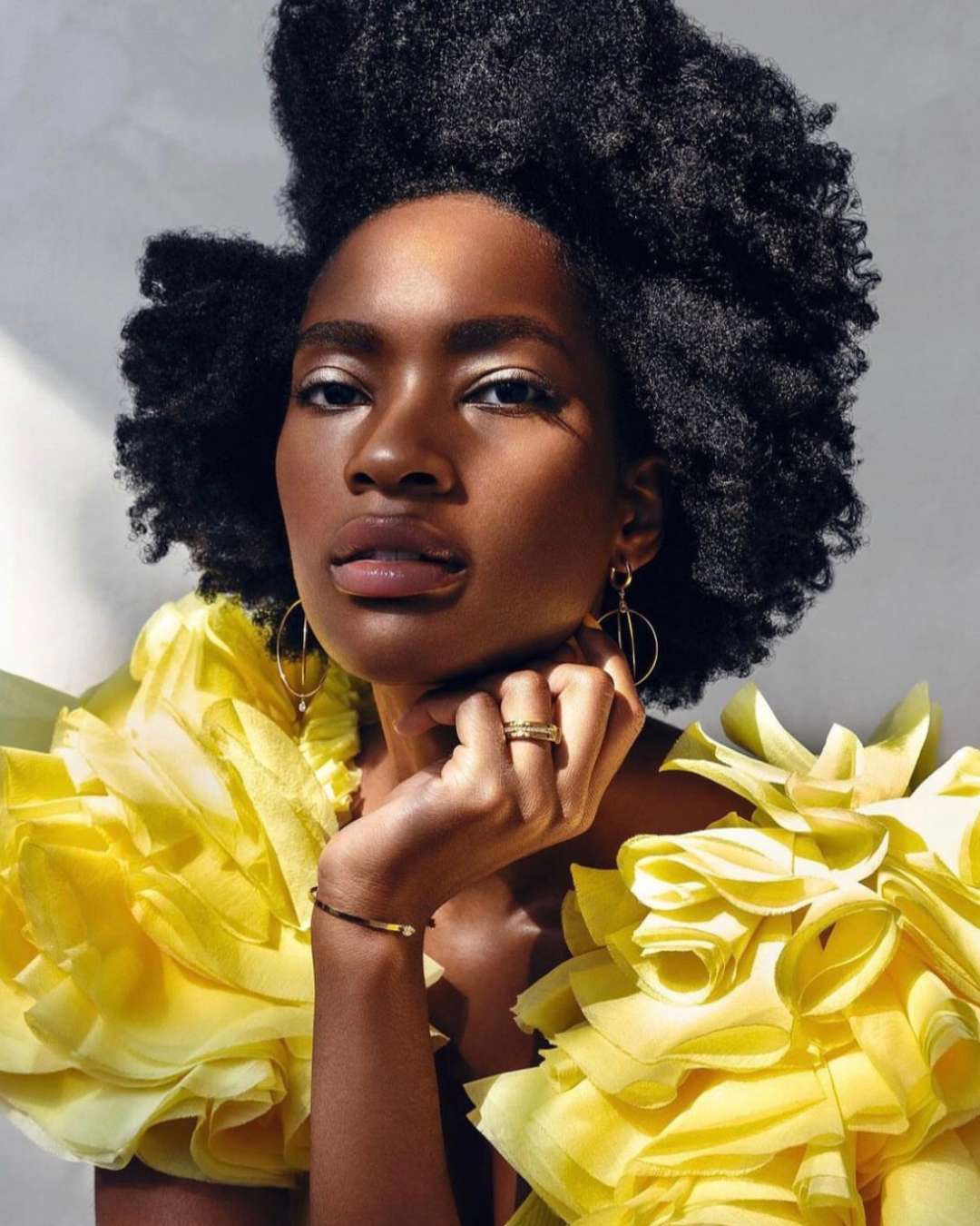 Woman wearing a yellow dress and gold jewelry with ruffled details against a neutral background - Camille Jewelry