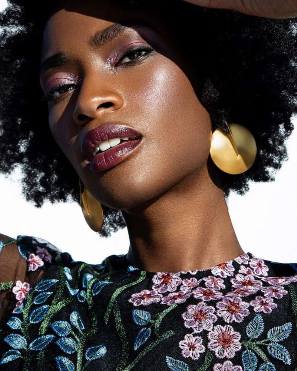 Woman with large hoop earrings by Camille Jewelry and floral embroidery on clothing against a blurred background. 