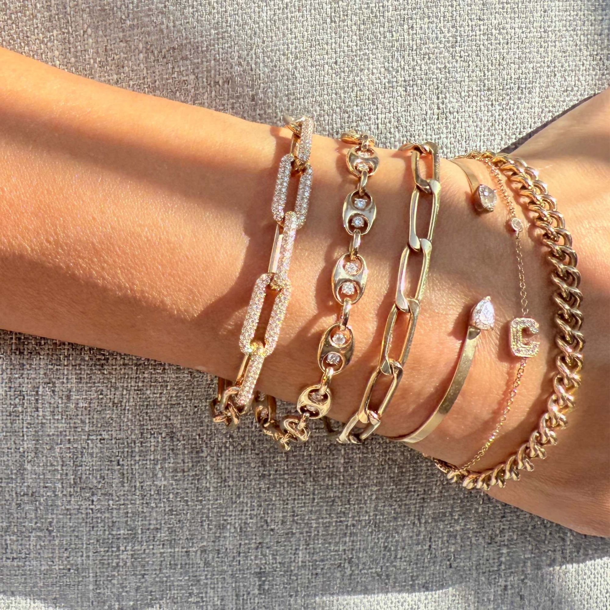Gold mariner bracelet on a wrist with other gold and diamond stack against a neutral background - Camille Jewelry