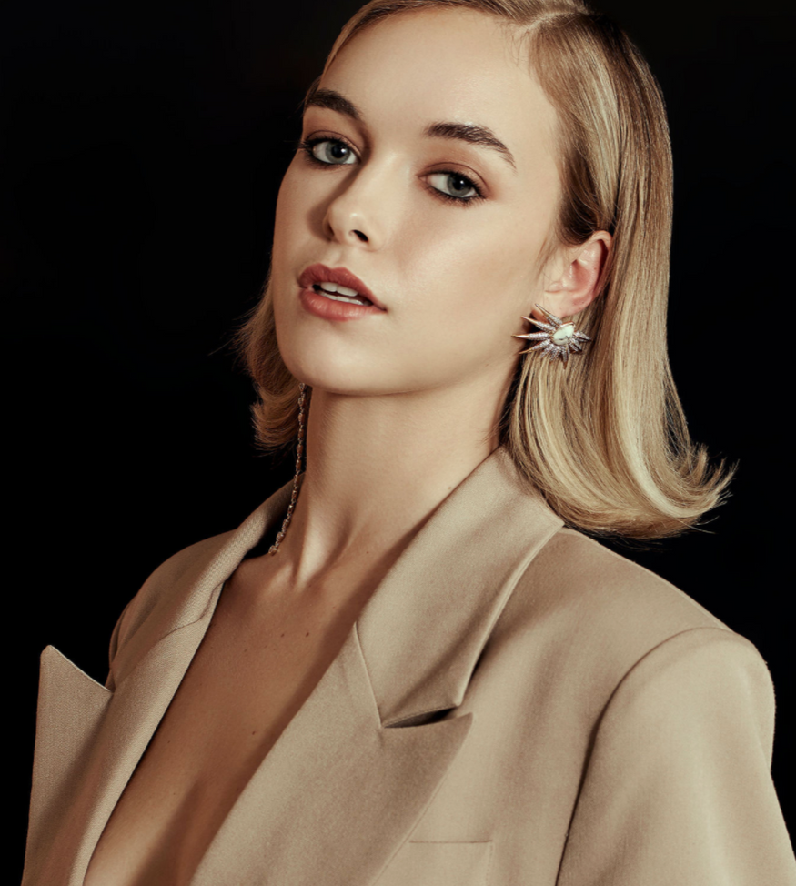 Woman wearing a beige blazer against a black background with Phoenix wing gold earrings | Camille Jewelry