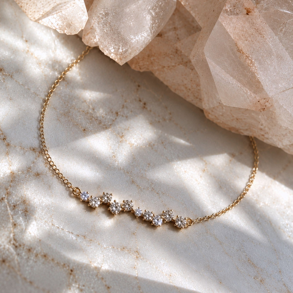 A delicate 14K gold chain bracelet with a row of small rund lab created diamond clusters, displayed on a light marble surface with soft shadows and pale crystal by Camille Jewelry