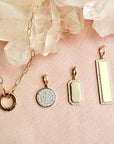 Diamond pavé disc charm in solid 14K gold shown alongside a paperclip chain necklace and two additional gold charms with diamond borders by Camille Jewelry.