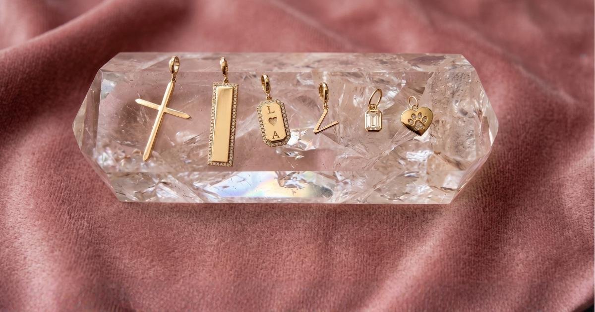 Six gold jewelry for women charms in solid 14k gold and diamonds displayed on a clear faceted crystal holder, set against a soft dusty pink suede background by Camille Jewelry. 