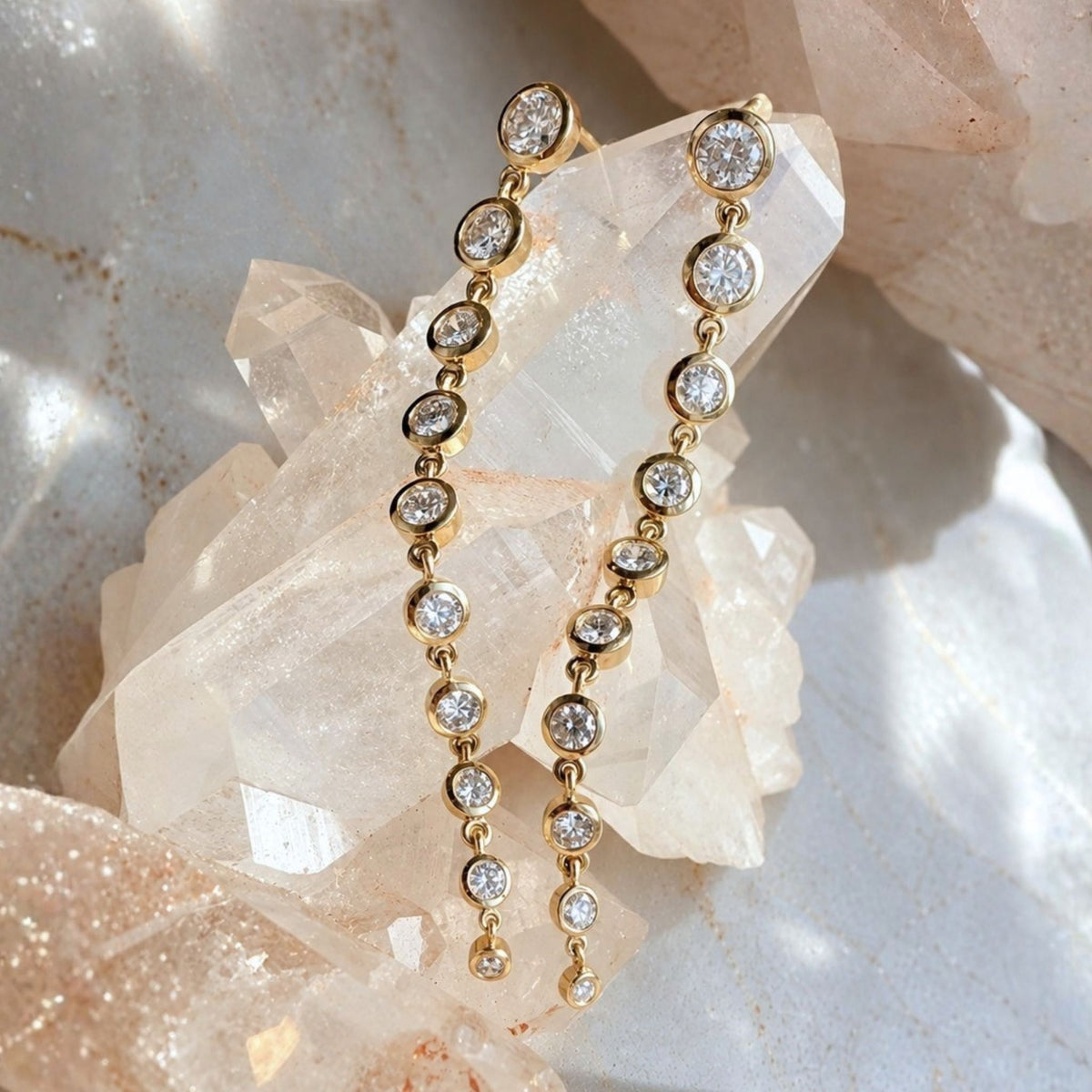 14K Gold graduated lab created diamond earrings displayed on a cluster of pale quartz crystals, by Camille Jewelry.