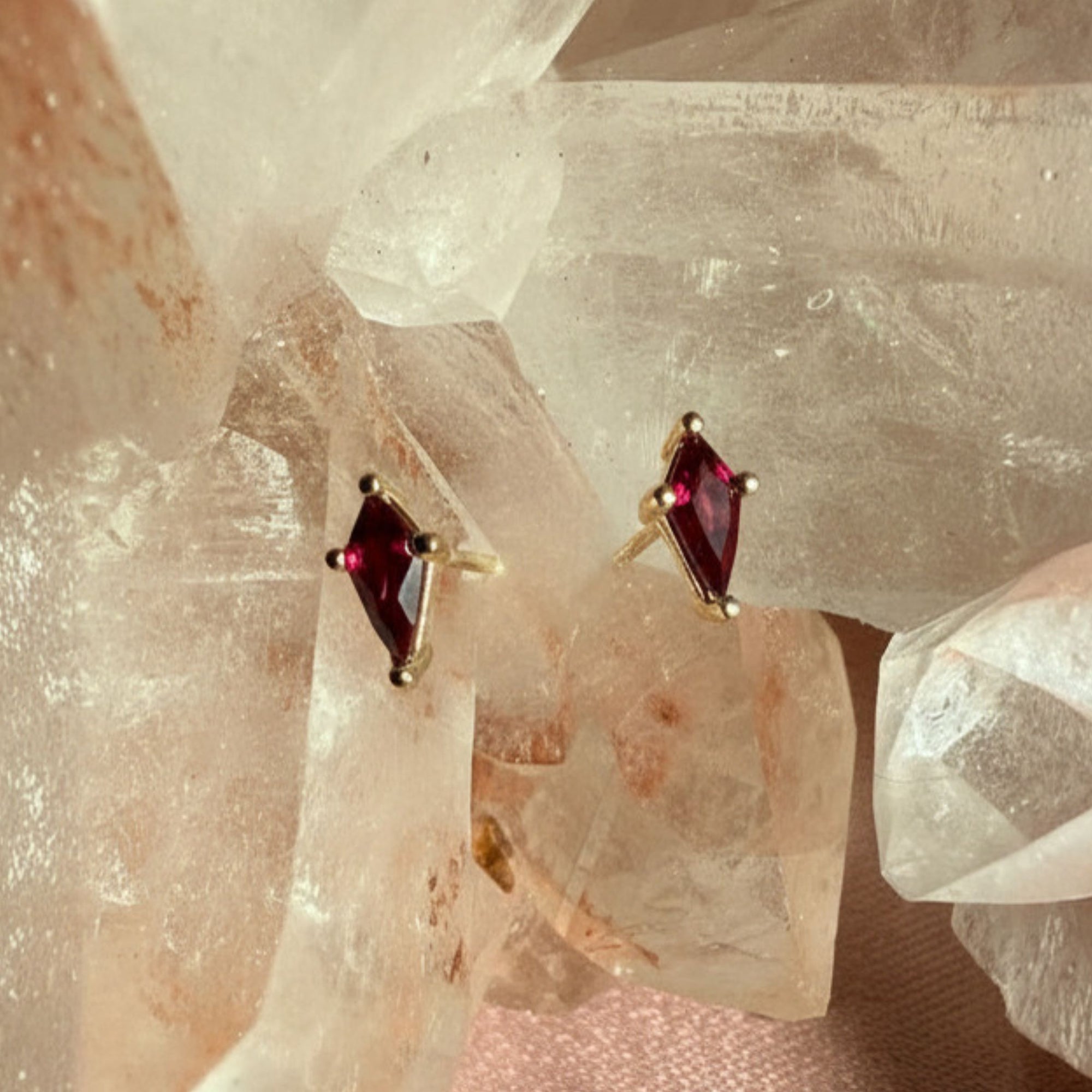 Pair of kite cut lab created ruby gemstone stud earrings in 14K yellow gold on a quartz crystal background by Camille Jewelry