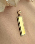 Close up of an engravable gold bar charm in 14K yellow gold with a natural diamond border and clip bail on pink fabric by Camille Jewelry