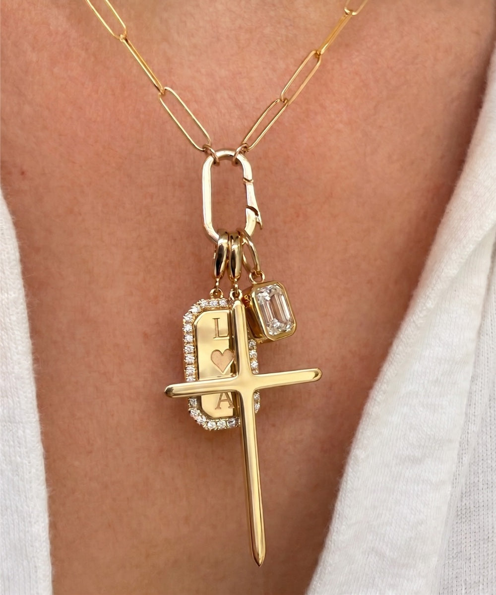 14k solid yellow gold charms on a diamond tag, cross and emerald cut diamond on a paperclip chain worn close up by Camille Jewelry. 