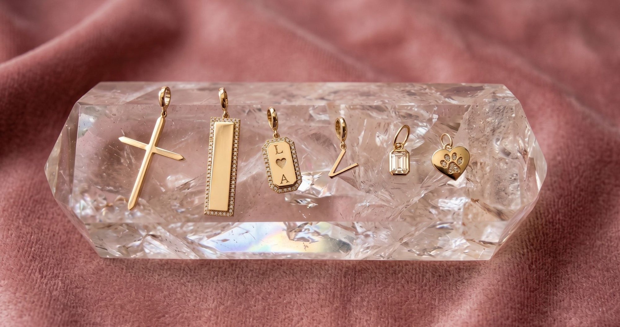 Gold charms that are in diamonds and personlized on a quartz display and soft pink background by Camille Jewelry