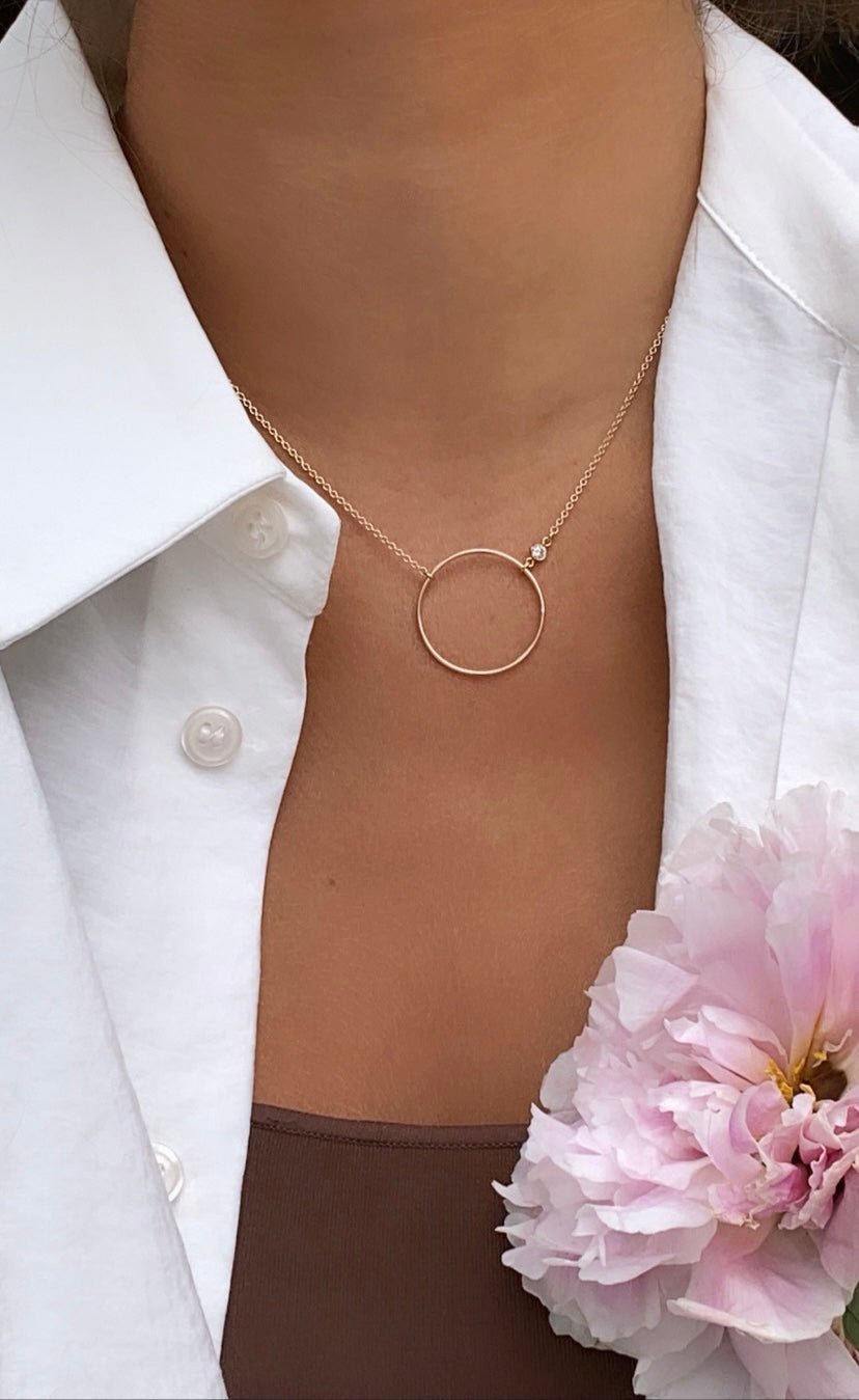 Close up of an open disk pendant with bezel set cubic zirconia on a gold filled rolo chain on model by Camille Jewelry