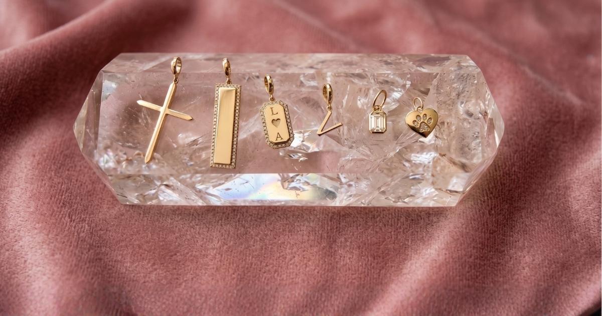 Gold jewelry for women of diamond and personalized charms on a quartz display and dusty pink fabric background for Camille Jewelry. 