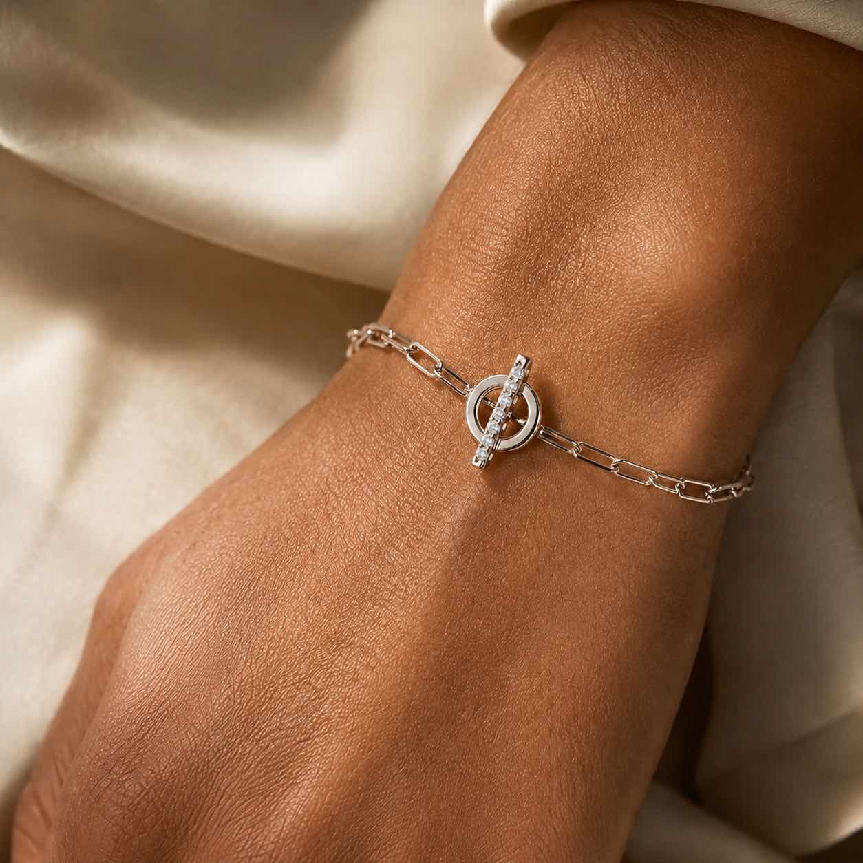 Woman wearing a gold toggle bracelet in 14K white gold with a diamond set bar on a neutral background by Camille Jewelry