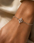 Woman wearing a gold toggle bracelet in 14K white gold with a diamond set bar on a neutral background by Camille Jewelry