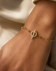 Woman wearing a gold toggle bracelet in 14K yellow gold with a diamond set bar on a neutral background by Camille Jewelry