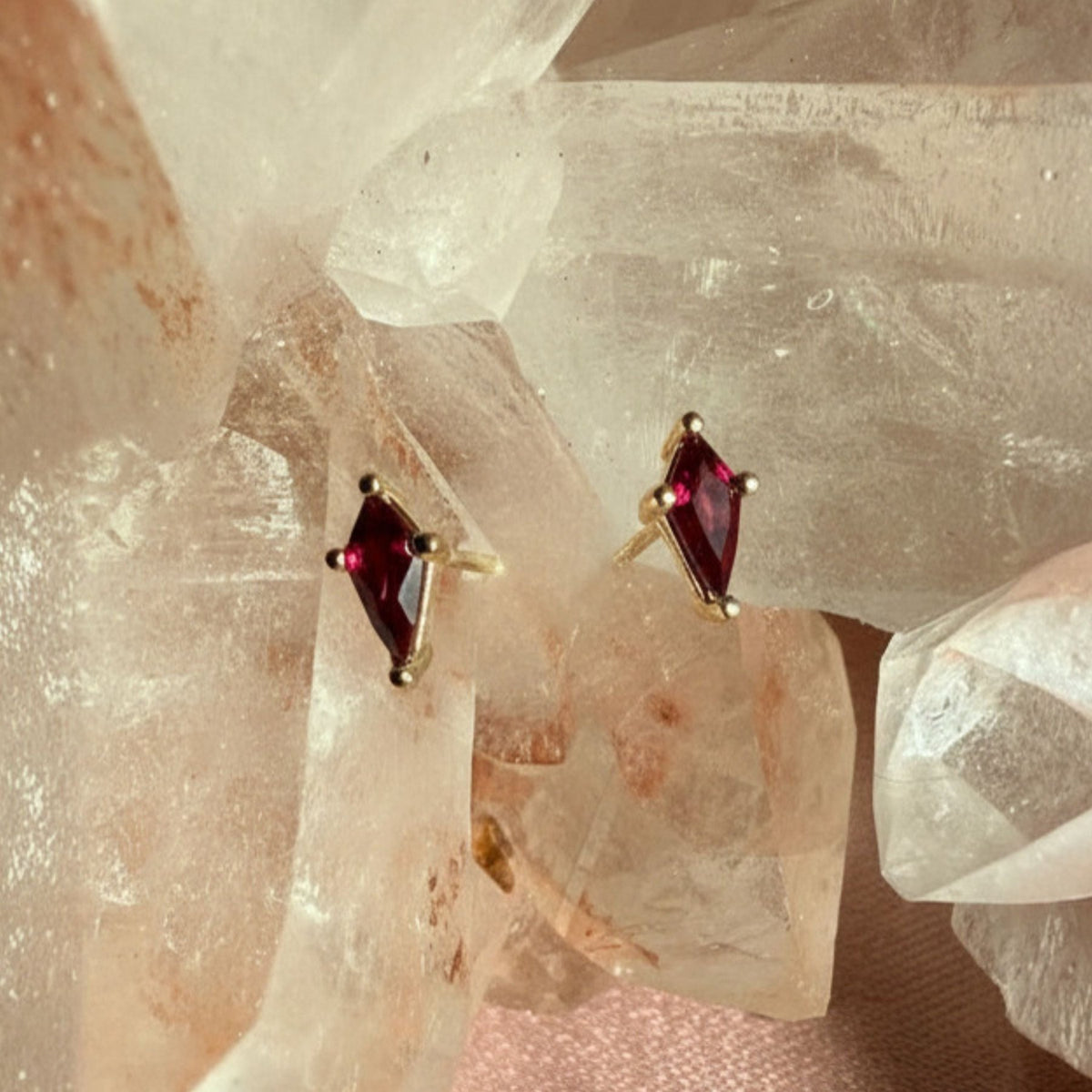 Pair of kite cut lab created ruby gemstone stud earrings in 14K yellow gold on a quartz crystal background by Camille Jewelry