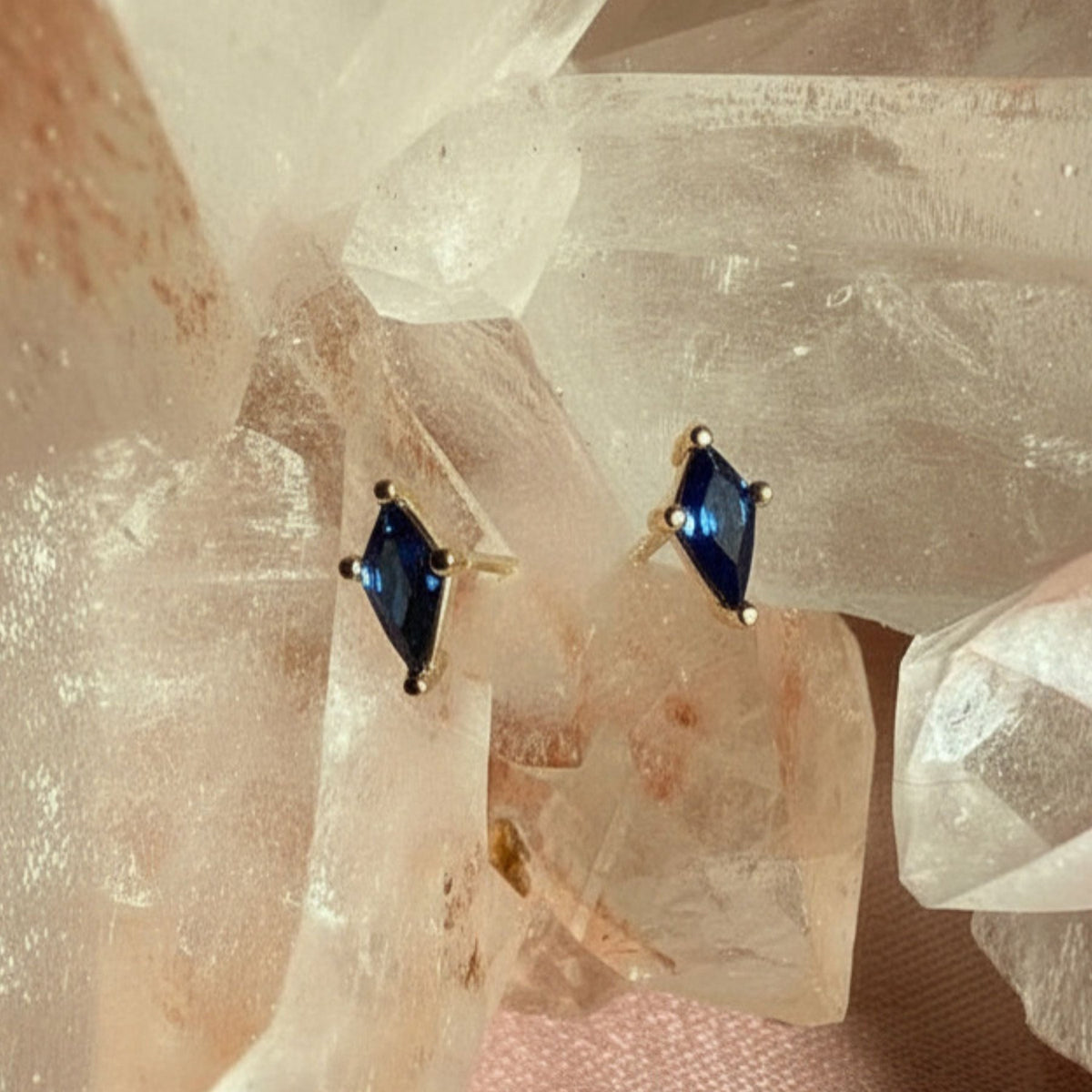 Pair of kite cut lab created sapphire gemstone stud earrings in 14K yellow gold on a quartz crystal background by Camille Jewelry