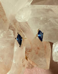 Pair of kite cut lab created sapphire gemstone stud earrings in 14K yellow gold on a quartz crystal background by Camille Jewelry