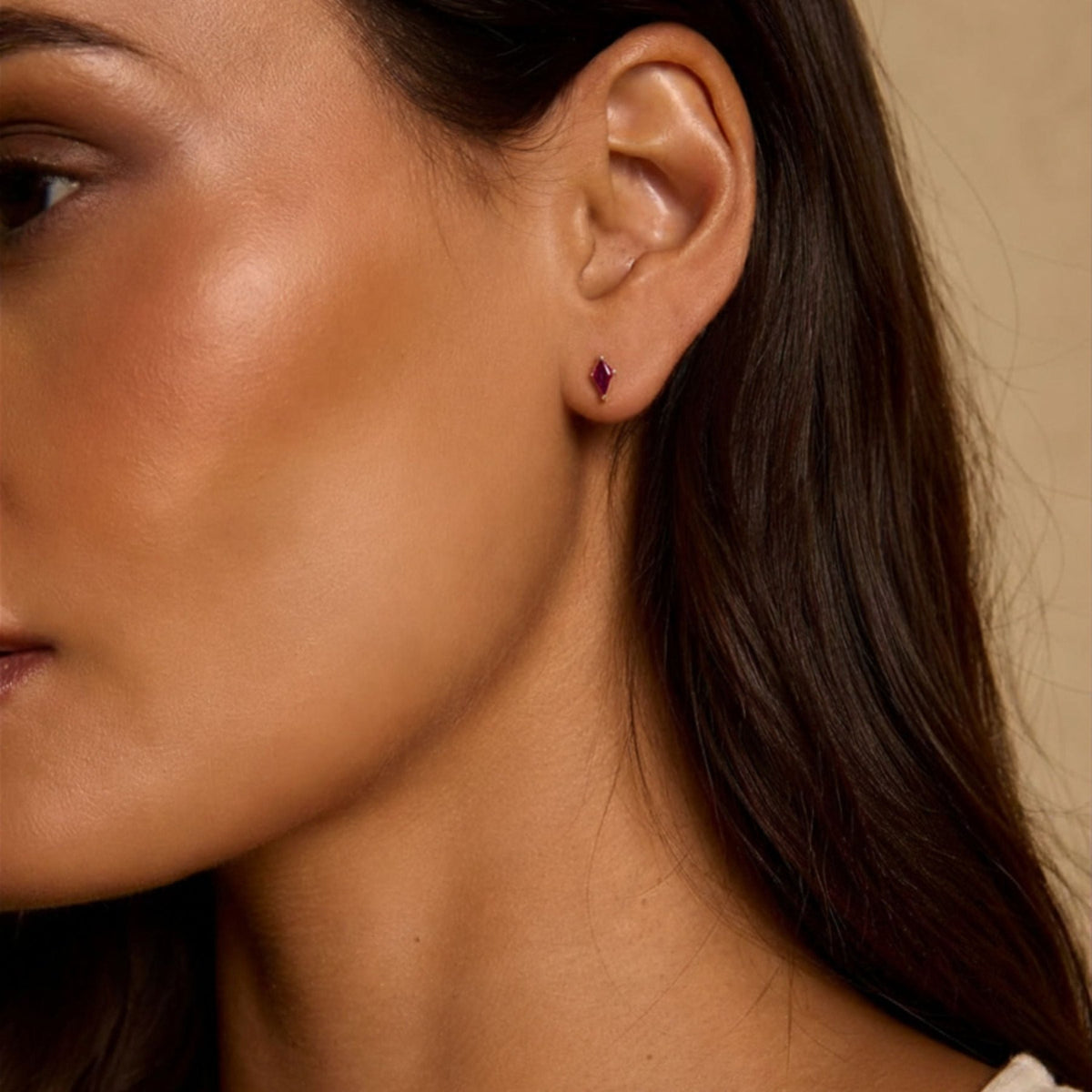 Woman wearing kite cut lab created ruby gemstone stud earrings in 14K yellow gold against a neutral background by Camille Jewelry