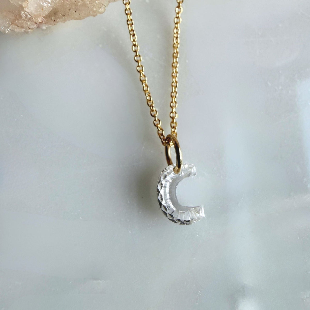 A 14k yellow gold chain necklace with a floating lab created diamond "C" initial charm, displayed on a pale marble surface, by Camille Jewelry. 