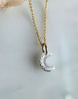 A 14k yellow gold chain necklace with a floating lab created diamond "C" initial charm, displayed on a pale marble surface, by Camille Jewelry. 